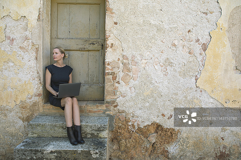 意大利，托斯卡纳，蒙特里吉奥尼，一个女人坐在门口用笔记本电脑图片素材