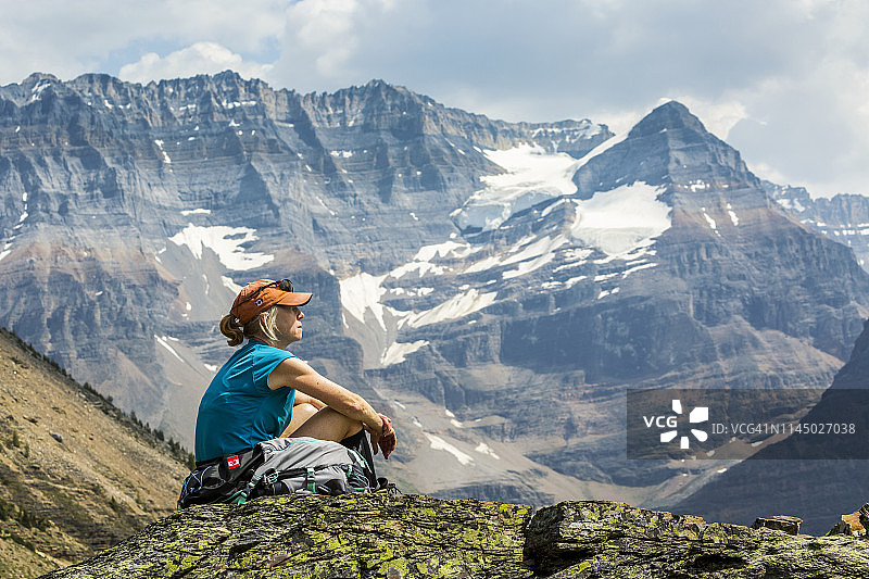女徒步旅行者坐在一个多岩石的地区，在背后俯瞰着山景图片素材