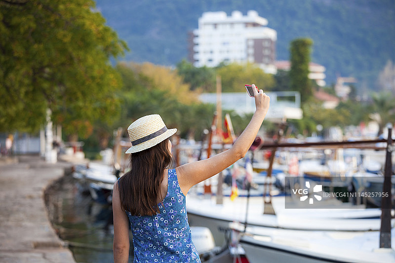 女人戴着帽子站在港口自拍的后视图图片素材