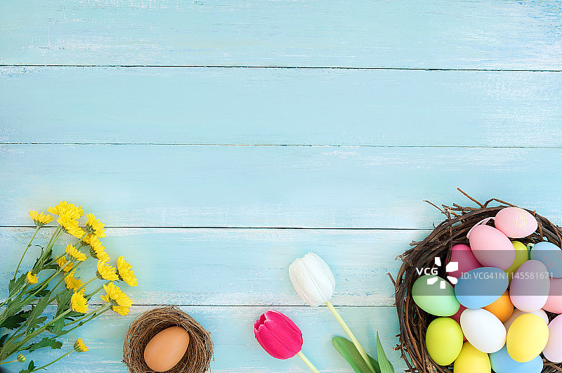 五颜六色的复活节彩蛋在巢与花在蓝色的木制背景。图片素材