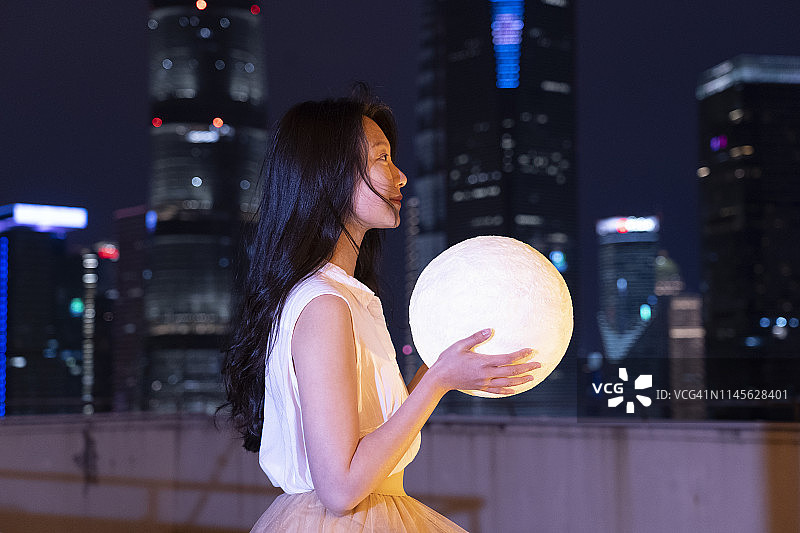 奇迹概念照片:一个亚洲女性抱着月亮等待童话故事发生在夜晚的城市图片素材