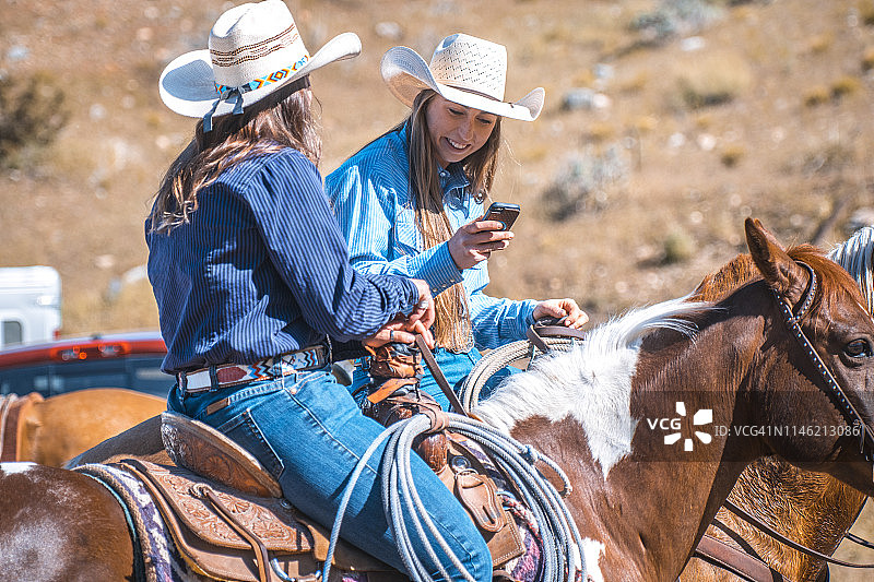 两个女西部牧场主在马背上聊天和分享电话照片图片素材