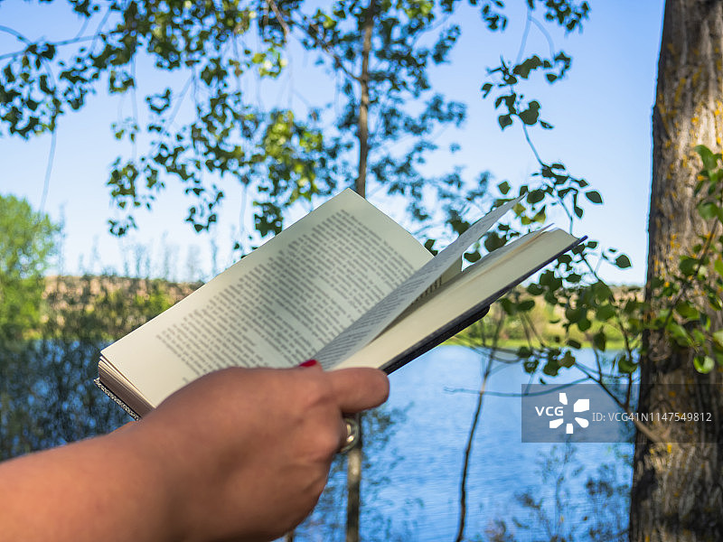 单打开书在一个人的手中在森林附近的一条河图片素材