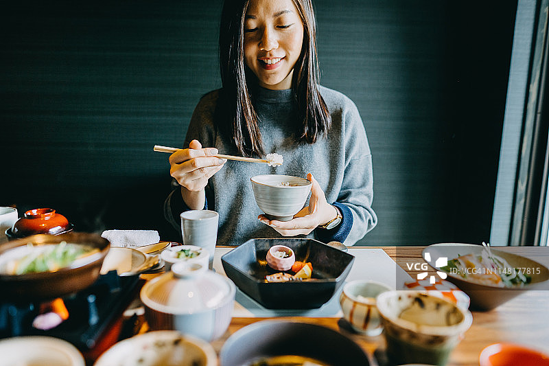 微笑的年轻亚洲女人享受精致的日式料理与各种配菜，海鲜和绿茶在餐厅图片素材