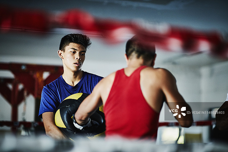 在拳击馆的训练中，男拳击手握着实心球，而搭档用拳头击打图片素材