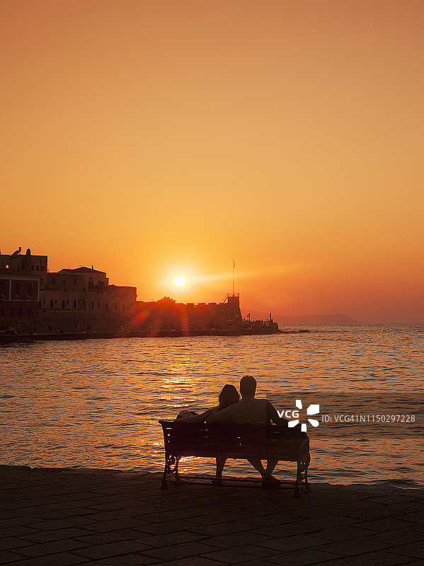 日落时分，一对情侣坐在长椅上。图片素材