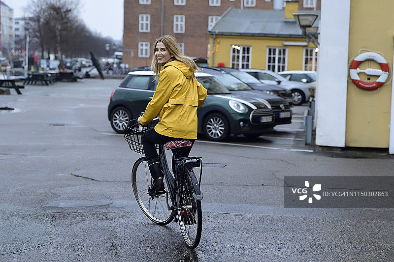 丹麦，哥本哈根，快乐的女人骑着自行车在海滨散步在雨天图片素材
