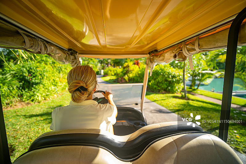 后视图女人驾驶高尔夫球车在热带岛屿图片素材