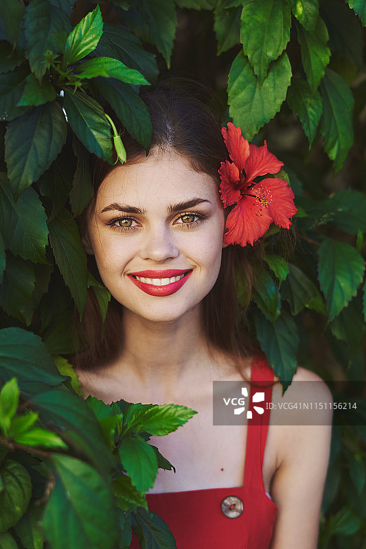 一个女孩在植物中的肖像，头上戴着一朵红色的花，看着相机微笑着图片素材