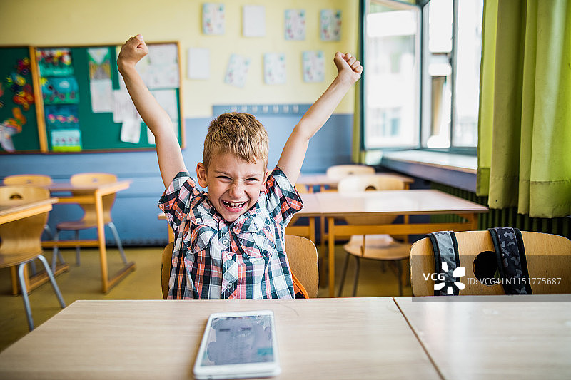 一个欢快的男生在教室里举起双臂庆祝。图片素材