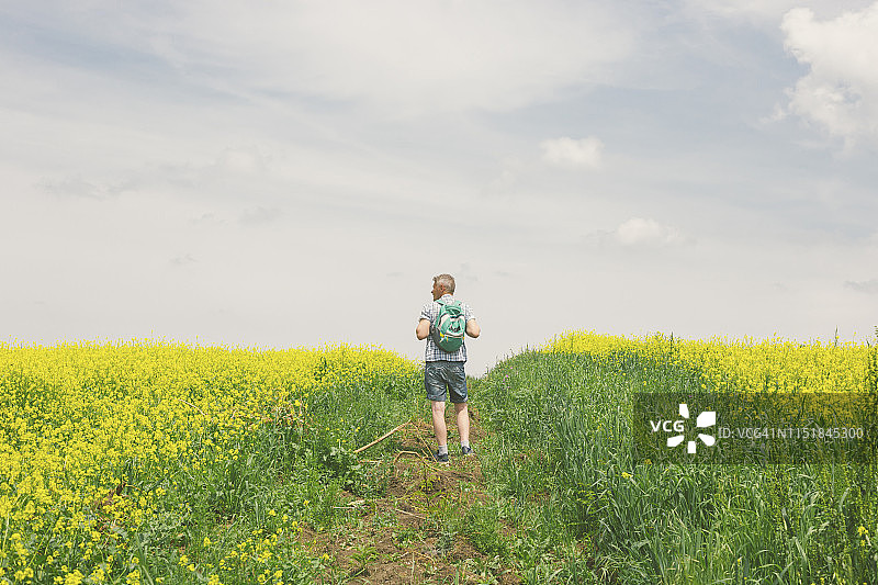 成年徒步旅行者喜欢在美丽的鲜花盛开的油菜花草地徒步旅行在春天。图片素材