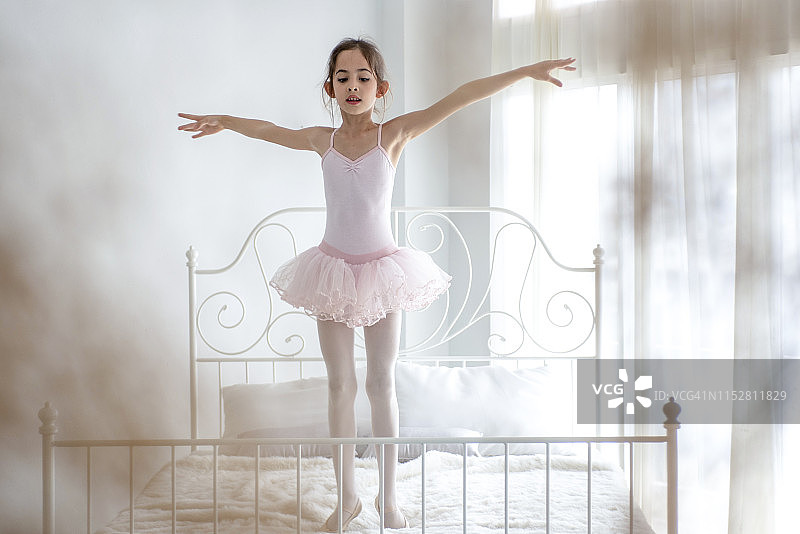 可爱的小女孩梦想成为一名芭蕾舞演员。穿着粉色短裙的小女孩在房间里跳舞。图片素材