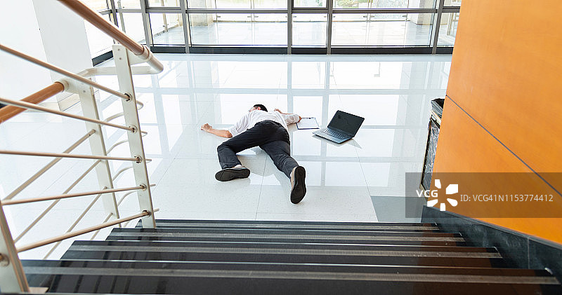 在现代办公大楼里，一名男子滑倒在潮湿的地板上。图片素材