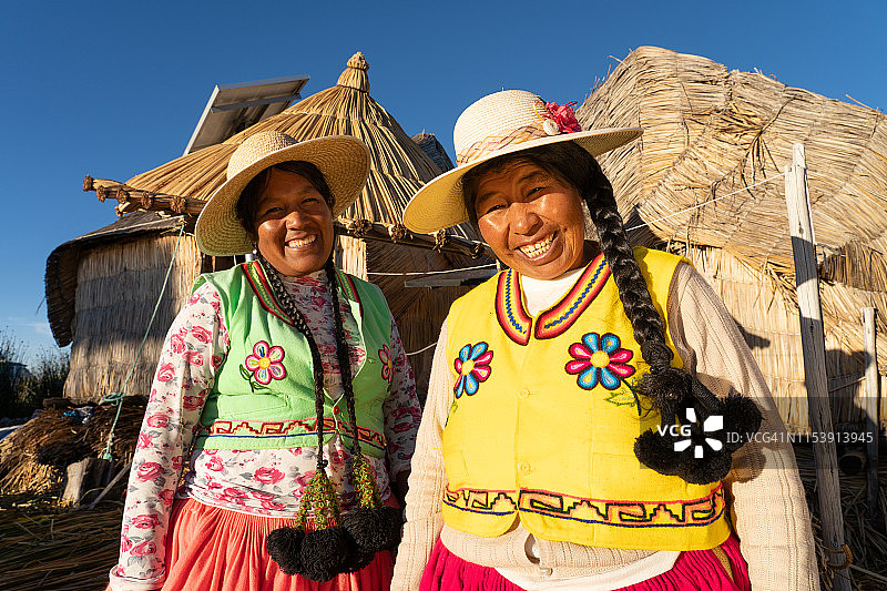 在秘鲁的喀喀湖普诺附近的浮动岛上，两名梳着辫子的乌鲁斯妇女穿着色彩鲜艳的当地传统服装。图片素材