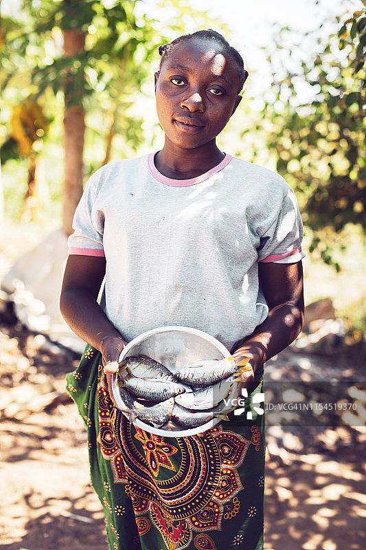 一位年轻的非洲妇女展示一碗鱼作为午餐图片素材