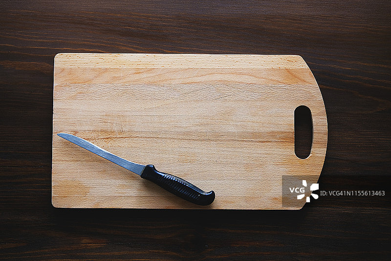 木切菜板上有黑色塑料柄的菜刀，特写。为文本复制空间。厨具的概念，烹饪。图片素材