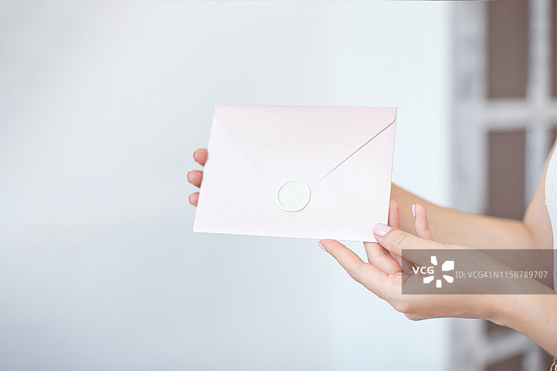 特写照片的女性手拿着一个银色的蓝色或粉红色的邀请信封蜡印章，礼品证书，一张明信片，婚礼请柬。图片素材