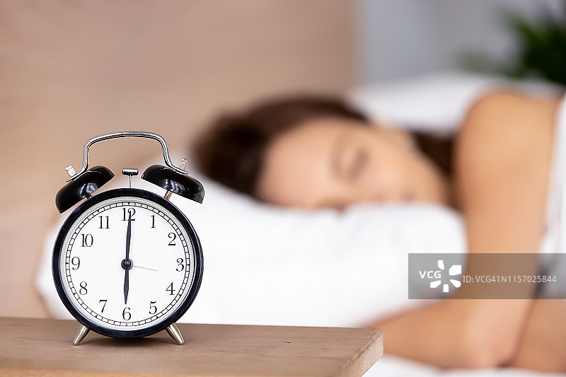 床头柜上的闹钟背景是一个女人正在睡觉图片素材