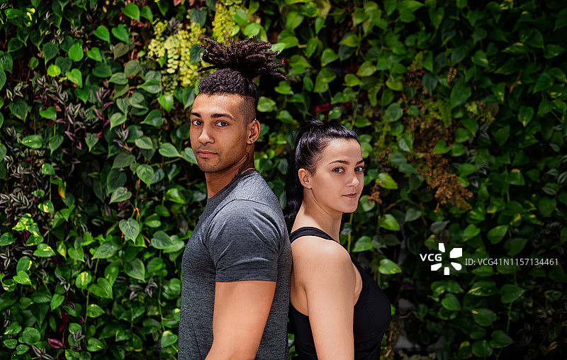 一对年轻夫妇背靠背站在户外，以绿色为背景。图片素材
