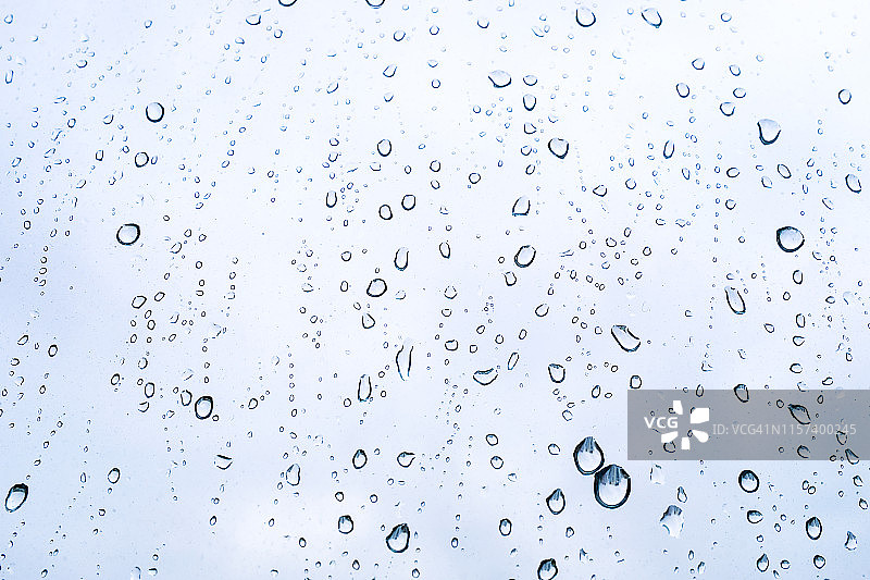 阴天，雨滴落在窗户上。下雨的天气，雨的背景和散景。阵雨过后，蓝色的天空映衬着窗户玻璃上的水滴。图片素材