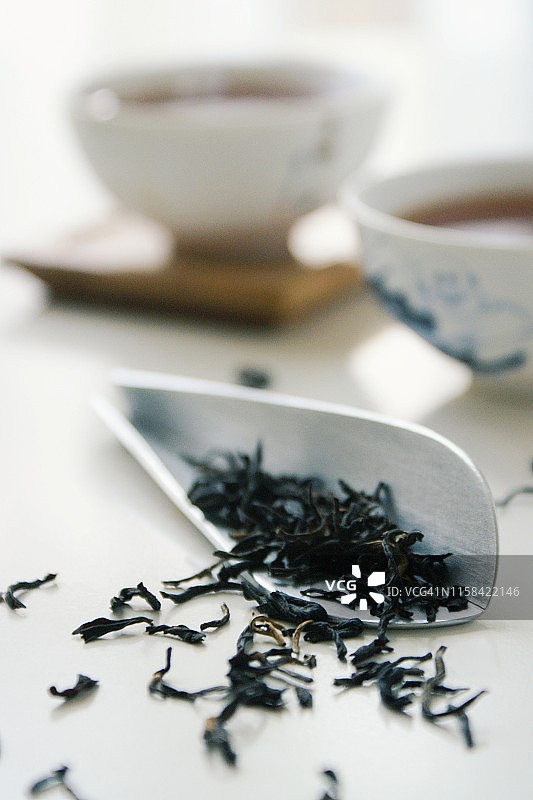 白色桌上放着斯里兰卡红茶的干叶子，背景是茶杯。图片素材