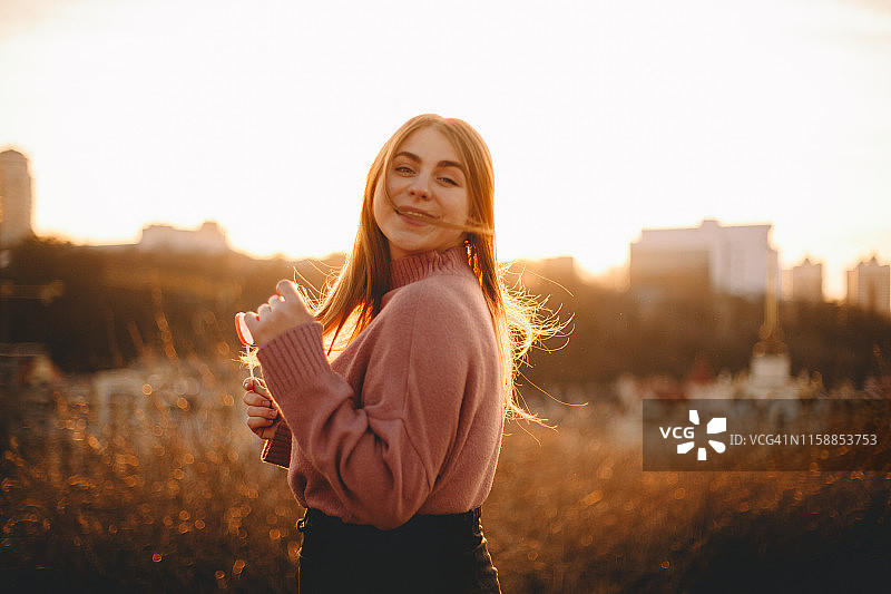 一个快乐的年轻女子站在日落的田野里的肖像图片素材