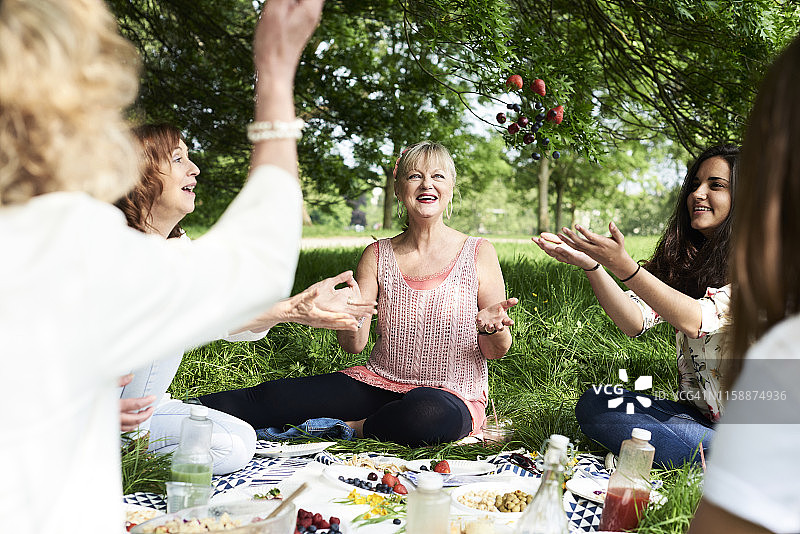 在公园野餐时，快乐的女人把浆果抛向空中图片素材