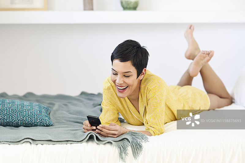 快乐的年轻女子在床上用手机图片素材