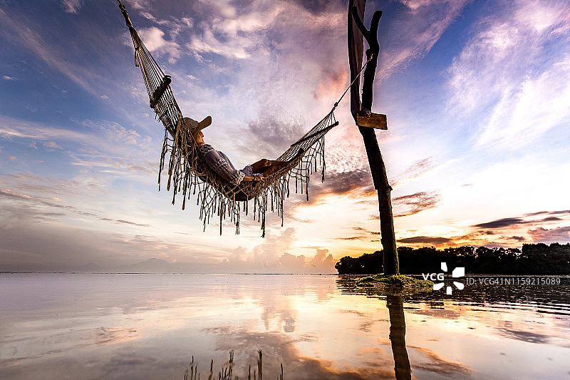 下图是一个女人在海面上的吊床上享受日落。图片素材