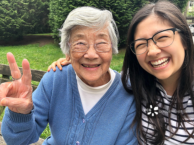 亚洲祖母和欧亚孙女在长凳上微笑拍照图片素材