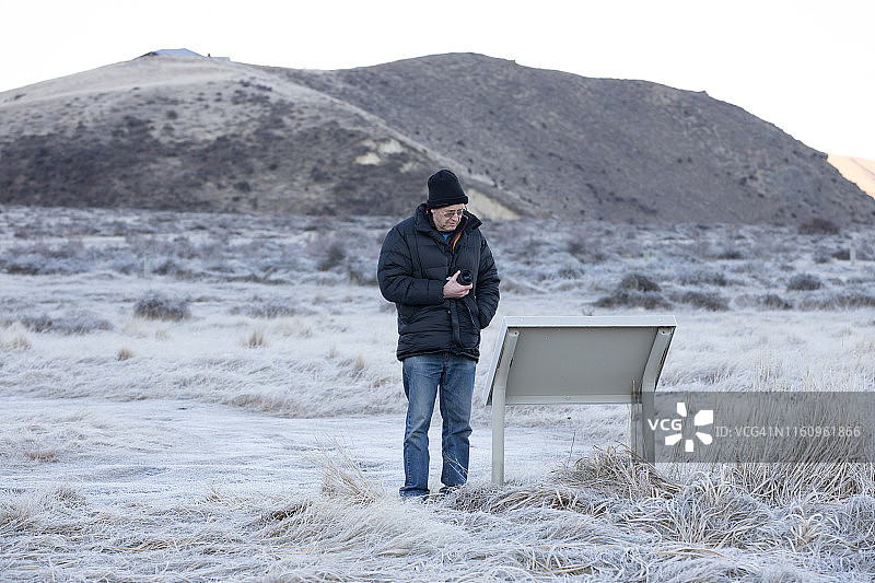 一个穿着暖和的人站在冰天雪地里看信息牌图片素材