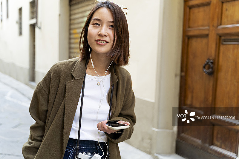 意大利，佛罗伦萨，一个年轻女子戴着耳机和手机在小巷里图片素材