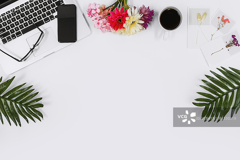 笔记本电脑，手机和热带树叶在白色的桌子上图片素材