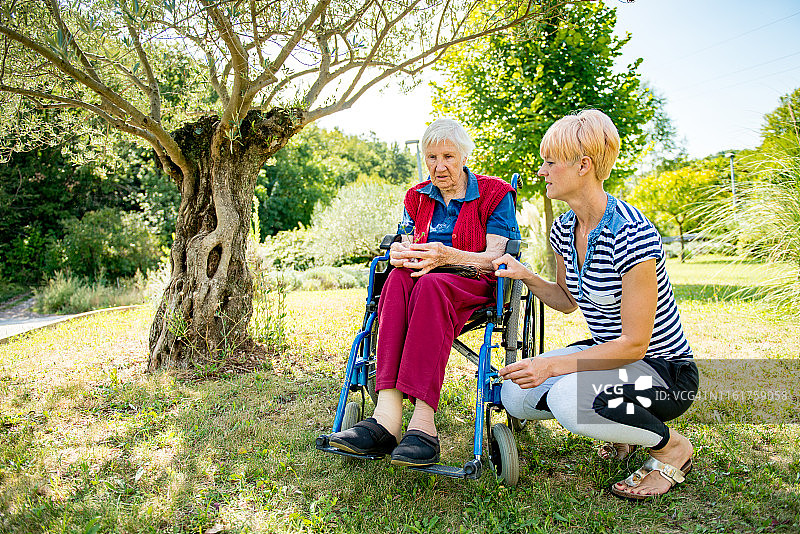 一位成年妇女与坐在轮椅上的老年妇女交谈图片素材