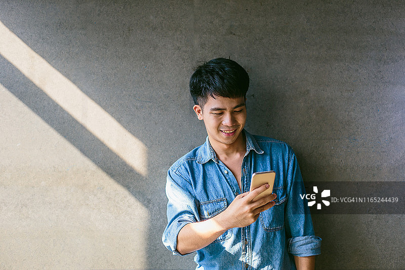 年轻的亚洲男子在办公室用灰色背景的智能手机图片素材