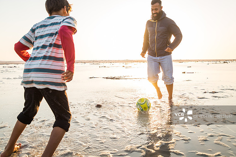 爸爸和儿子在沙滩上踢足球图片素材