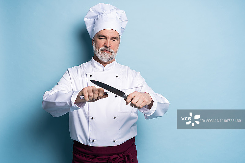 一个成熟的厨师厨师的肖像拿着刀孤立在一个蓝色的背景。图片素材