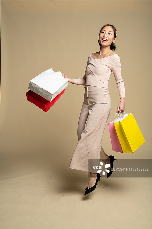 一位年轻的亚洲妇女穿着休闲服装，拿着五颜六色的购物袋图片素材