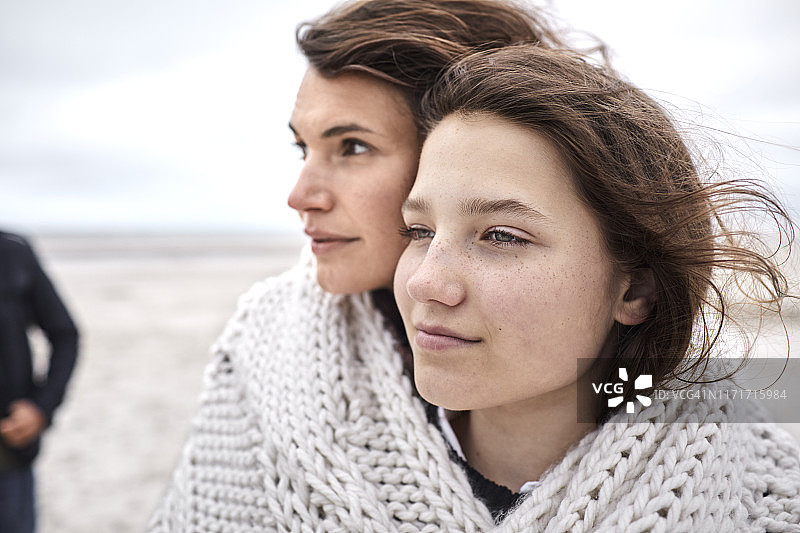 沙滩上，一个年轻的女人和一个女孩裹着毯子图片素材