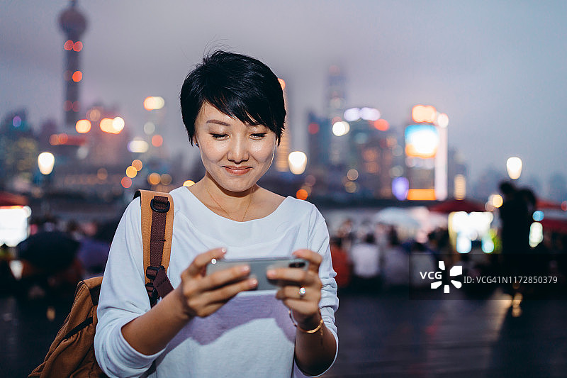 中国上海陆家嘴金融区的摩天大楼里，一名亚洲女性正在繁忙的市中心使用手机。图片素材