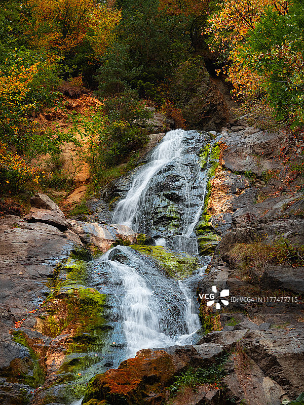 长曝高的梦幻般的瀑布正流淌在五彩斑斓的秋天森林里的岩石上图片素材