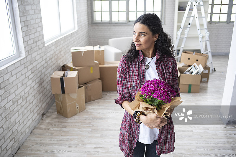 一个女人站在空荡荡的公寓里，手里拿着花图片素材