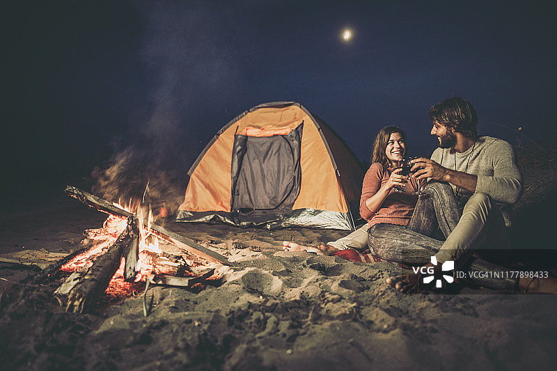 幸福的夫妇在露营之夜在火旁举杯共饮。图片素材