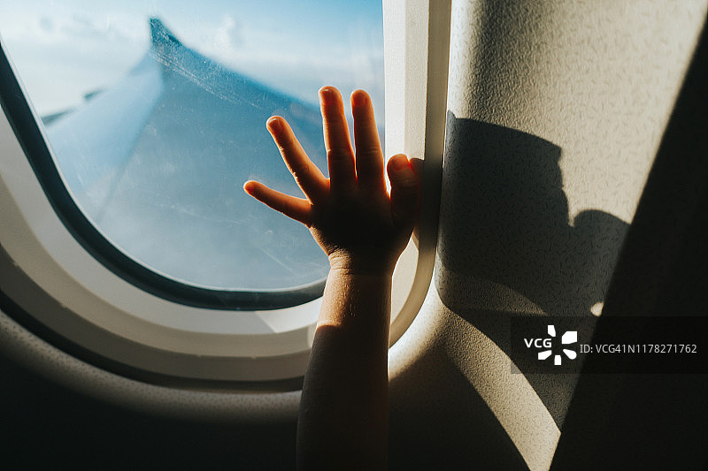 一个蹒跚学步的孩子在旅行时用手触碰蓝天下的飞机窗户图片素材