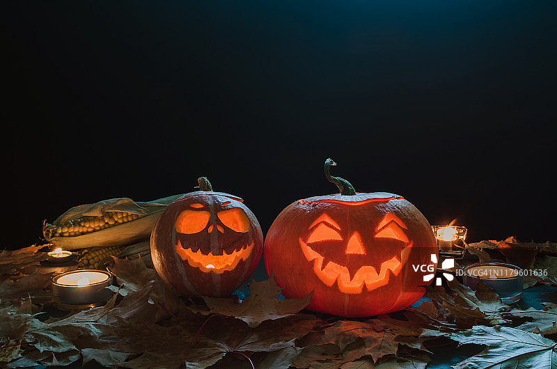 万圣节南瓜头杰克与蜡烛灯笼在黑暗的背景与秋天的树叶和玉米图片素材