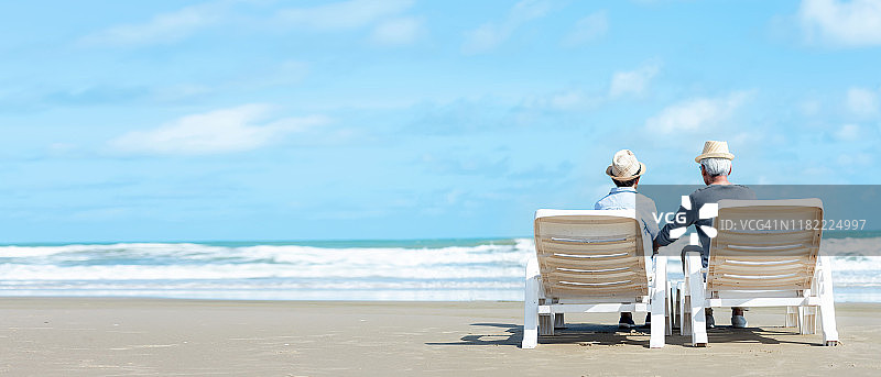 亚洲生活方式资深夫妇坐在放松和寒冷的海滩上快乐的爱情浪漫的夏天。老年家庭旅游，退休后的度假和夏季休闲活动。复制空间和本纳文本图片素材