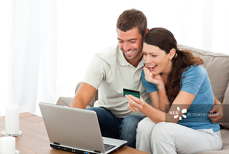 一对快乐的夫妇坐在沙发上用笔记本电脑在网上购物图片素材
