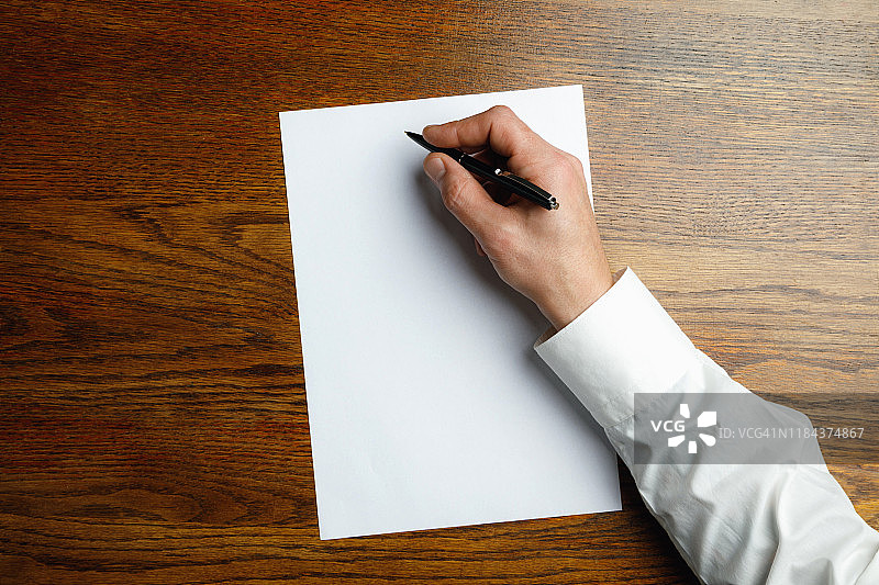 男性手握笔和书写在空白纸上木质背景上的文字或设计图片素材