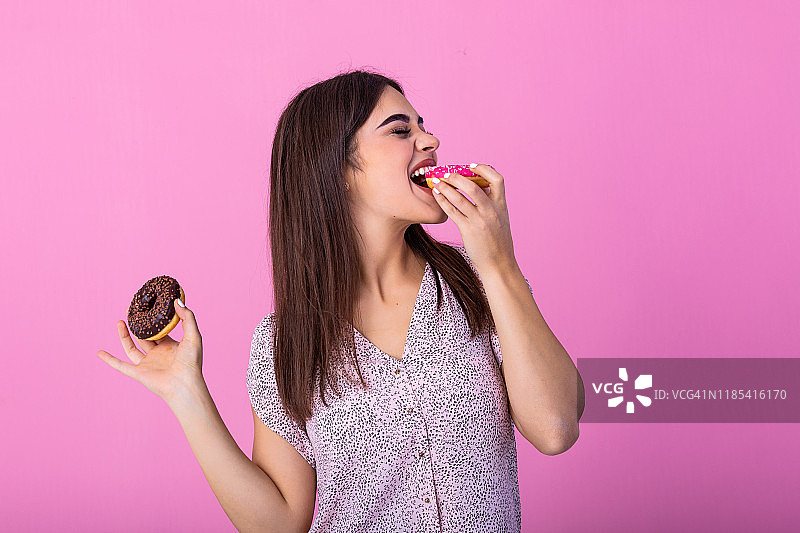 美女模特女孩吃五颜六色的甜甜圈。有趣的快乐风格的女人选择糖果在粉红色的背景。饮食,饮食的概念。垃圾食品，减肥，减肥图片素材