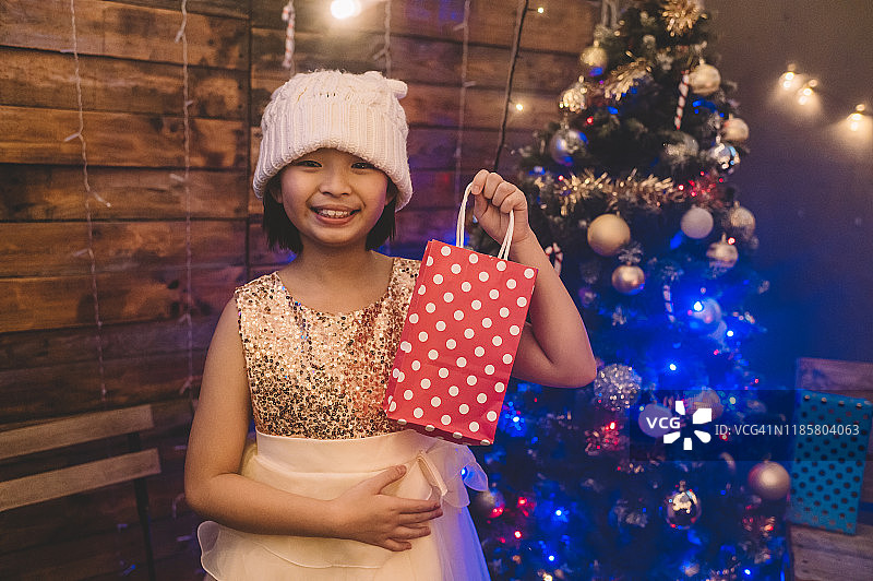 一个亚洲的中国小女孩收到了她的圣诞礼物，站在圣诞树旁看着镜头图片素材